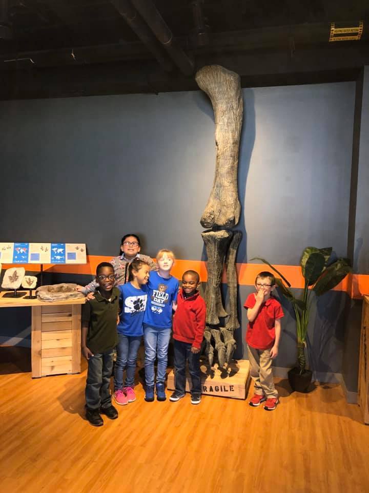students in front of large dinosaur fossil display
